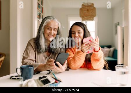Happy grandmother and granddaughter using smart phone at home Stock Photo