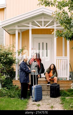 Happy multi-generation family waiting with luggage outside house Stock Photo