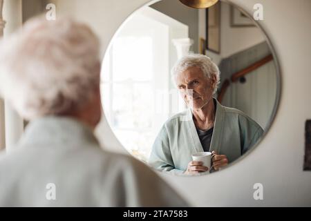 Senior man holding coffee cup while looking in mirror at home Stock Photo