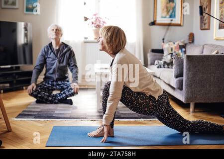 Senior woman and man practicing yoga together in living room at home Stock Photo