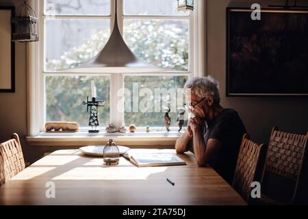 Senior man with eyeglasses reading book on table at home Stock Photo