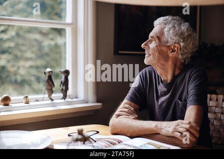 Contemplative senior man looking through window at home Stock Photo