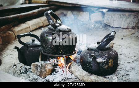 Coffee pot on campfire. Kettle is heated on a bonfire. Outdoor recreation concept. Close up boil water old kettle on the fire with a charcoal stove at Stock Photo