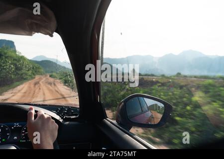 View from the car windshield from the driver's seat. Travel in spring or summer weather. Beautifull view of the car side mirror. Dirty Rural Road In S Stock Photo