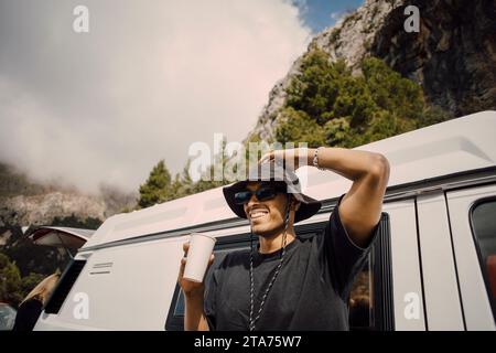 Smiling young man with head in hand holding drink glass near van Stock Photo