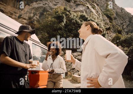 Happy multiracial male and female friends talking while having drinks during road trip Stock Photo