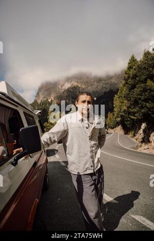Young man leaning on van during road trip Stock Photo