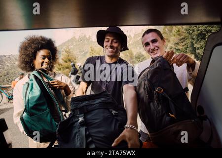 Happy male and female friends unloading luggage from van trunk during road trip Stock Photo