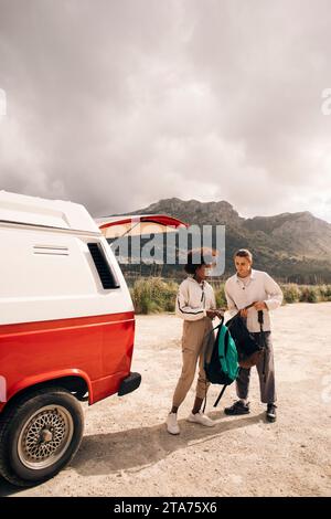 Male and female friends holding backpacks while standing near van against mountains Stock Photo