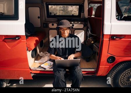 Smiling young man using laptop while sitting in van during road trip Stock Photo