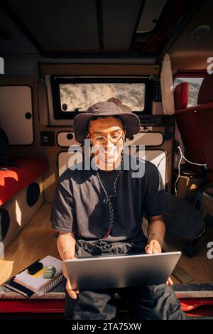 Happy young man using laptop while sitting in van during vacation Stock Photo