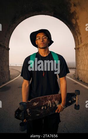 Portrait of young man holding skateboard while standing in tunnel Stock Photo