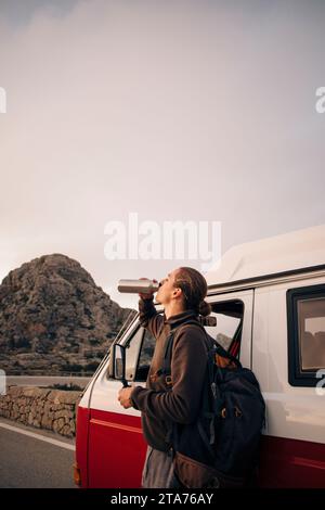 Young man drinking water while standing near van on vacation Stock Photo