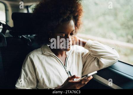 Young afro woman using smart phone while sitting in van during road trip Stock Photo