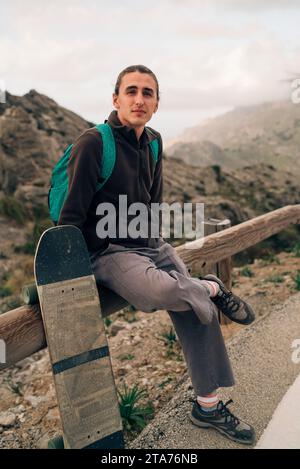 Portrait of young man sitting on railing by skateboard Stock Photo