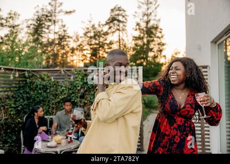 Happy woman dancing with young male friend while celebrating during dinner party Stock Photo