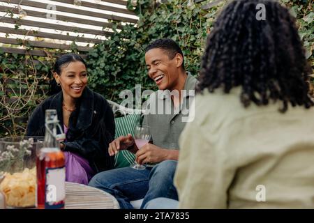 Young man laughing while enjoying drinks with female friends at dinner party Stock Photo