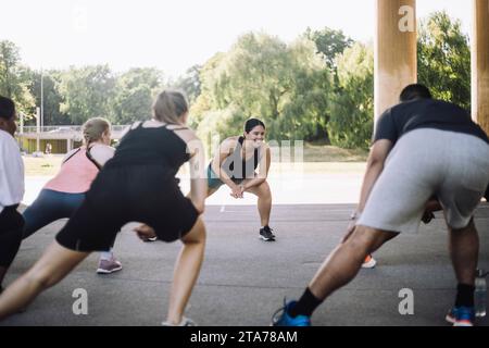 Smiling woman doing stretching with male and female friends during training class Stock Photo