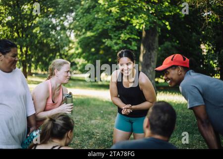 Happy woman talking with male and female friends after working out at park Stock Photo
