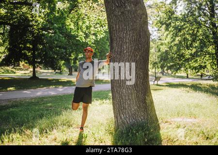 Man doing stretching while standing near tree at park on sunny day Stock Photo
