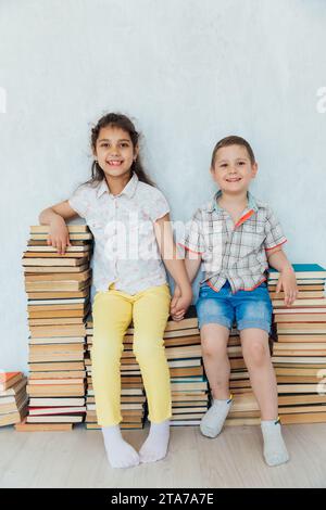 Boy and girl sitting on stacks of educational books Stock Photo