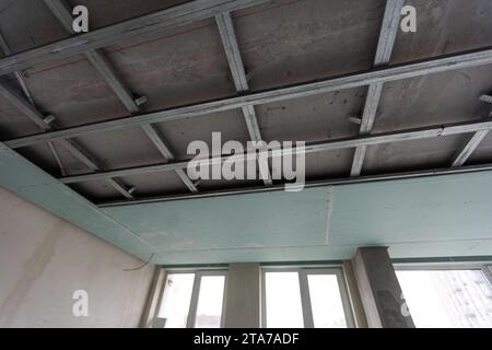 Installation of drywall. Workers are using screws and a screwdriver to attach plasterboard to the ceiling Stock Photo