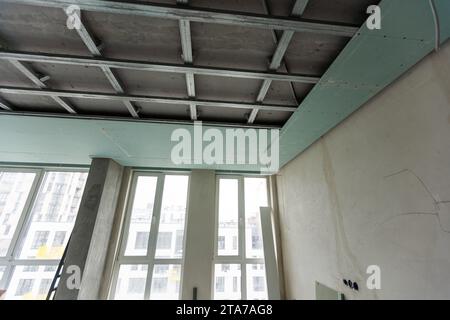 Installation of drywall. Workers are using screws and a screwdriver to attach plasterboard to the ceiling Stock Photo