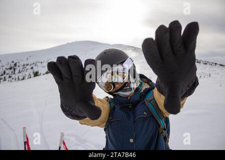 A skier in warm black gloves, arms extended forward, obscuring the sun and part of the face in ski goggles and a helmet. Winter equipment ski resort, Stock Photo