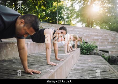 Portrait of smiling woman doing push-ups with friends on steps at park Stock Photo