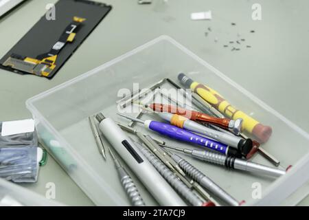 A semi-transparent plastic box full of small screwdrivers for repairing electronic components on the table in a mobile phone repair shop Stock Photo