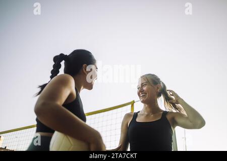 Low angle view of happy female friends talking while playing volleyball against sky Stock Photo