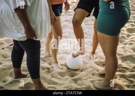 Low section of female friends standing on sand with volleyball Stock Photo