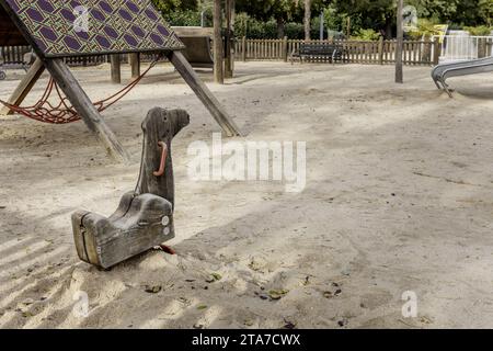 A wooden children's game in the shape of a dromedary head inside a playground with sand floors and wooden games Stock Photo