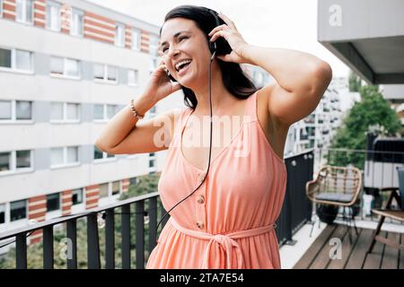 Happy woman enjoying listening to music through headphones in balcony Stock Photo