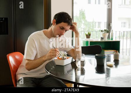 Upset man leaning on elbow having meal while sitting at table in home Stock Photo