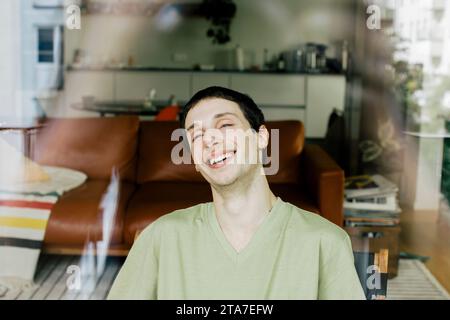Happy young man enjoying at home seen through glass window Stock Photo