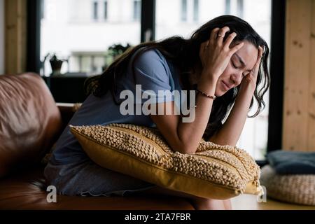 Frustrated young woman with head in hands sitting on sofa at home Stock Photo