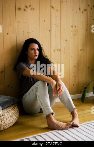 Depressed woman sitting near wooden wall at home Stock Photo