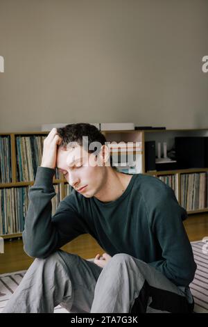 Upset young man with head in hand sitting at home Stock Photo