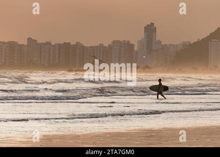 City of Santos, Brazil. Surfer entering the water. Golden hour on Santos beach, Urubuqueçaba Island, Emissary Park with a sculpture by Tomie Ohtake. Stock Photo
