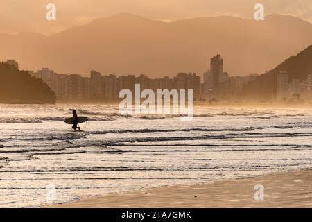 City of Santos, Brazil. Surfer entering the water. Golden hour on Santos beach, Urubuqueçaba Island, Emissary Park with a sculpture by Tomie Stock Photo