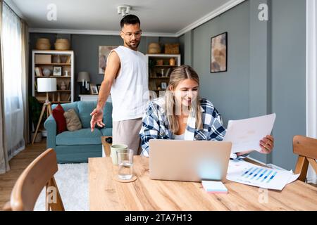 Young freelance woman remote working at home on laptop computer with boyfriend support. Business couple small online company owners research on intern Stock Photo