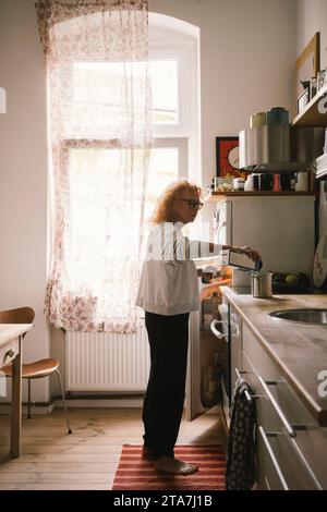 Side view of senior woman pouring milk in container while standing in kitchen at home Stock Photo