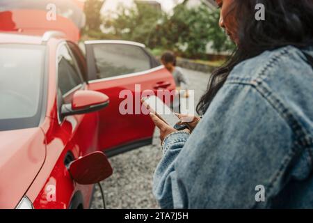Woman using smart phone next to electric car Stock Photo