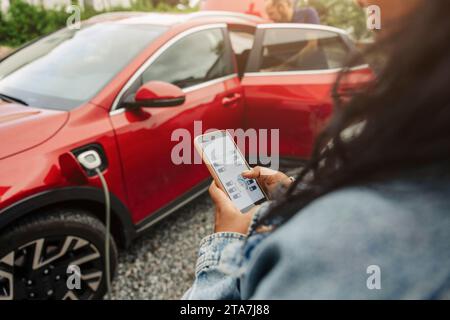 Woman using mobile app on smart phone near electric car Stock Photo
