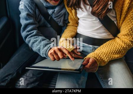 High angle view of girl using tablet PC with sister sitting in car Stock Photo