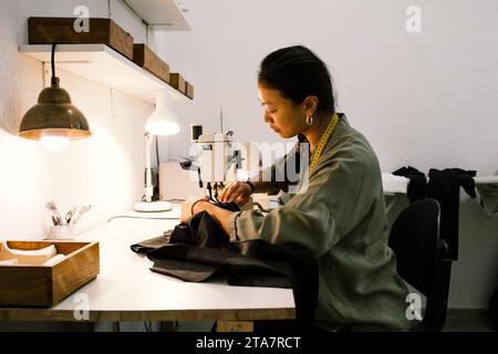 Side view of young seamstress making dress using sewing machine while working at store Stock Photo
