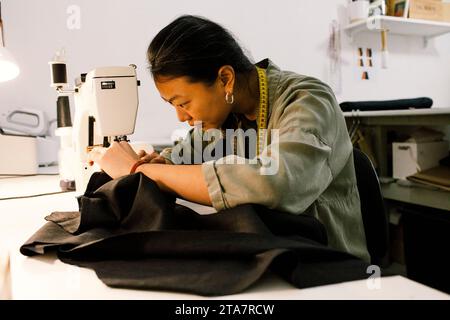 Focused seamstress stitching clothes using sewing machine while working at store Stock Photo
