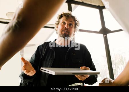 Frustrated man holding damaged laptop while talking with technician at store Stock Photo