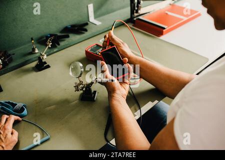 High angle view of male technician examining smart phone using multimeter at repair shop Stock Photo
